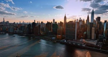 Güneş modern New York 'un siluetinin arkasında saklanıyor. Tekneler Doğu Nehri 'nin kıyısında yüzer. Hava perspektifi.