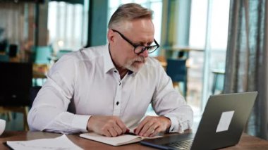 Beyaz gömlekli ve gözlüklü, gülümseyen bir iş adamı dizüstü bilgisayarına daha yakın duruyor. Şaşkın adam bilgisayar ekranına bakar.