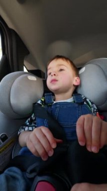 Kot pantolonlu beyaz bir erkek bebek arabaya biniyor. Çocuk bebek arabasının koltuğunda güvenli ve rahat bir şekilde oturuyor. Düşük açı. Dikey video.