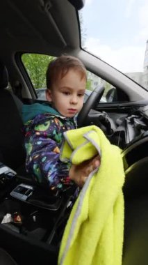 Küçük bebek arabada oturmuş panellerin tozunu alıyor. Güzel çocuk, arabayı temizliyor. Dikey video.