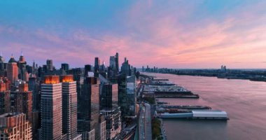 Gökyüzünde gün batımının pembe ışığı, Doğu Nehri 'nin su manzarası ve binaların cepheleri. Gün batımında New York manzarası. İnsansız hava aracı görüntüleri.