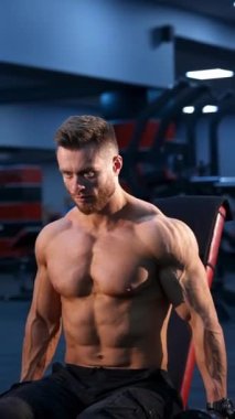 Halterle egzersiz yapan yakışıklı atletik vücut geliştirici. Spor salonunun arka planında kaslı vücut. Dikey video