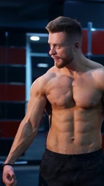 Güçlü kaslı sporcu antrenmandan sonra spor salonunda kas pompalıyor. Güçlü karın kasları olan mükemmel bir gövde. Çıplak gövdeli yakışıklı bir erkek. Dikey video