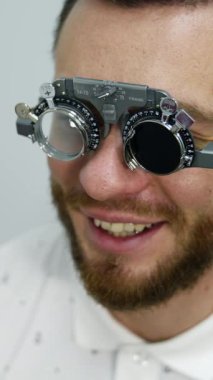Düzeltici test gözlükleriyle gülümseyen mutlu erkek hasta. Klinikteki görme duyusunu kontrol ediyorum. Göz doktorunda yakışıklı bir hastaymış. Dikey video