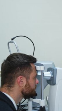 Görme düzeltmesi için göz hekimliği kliniğinde özel ekipman. Teknolojik olarak güncel ekipmanlar için özel düzeltici. Klinikte bir adamın portresi. Dikey video