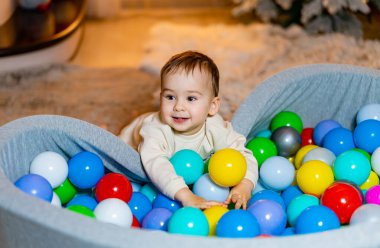 Toddler playing joyfully in colorful ball pit at home in the evening. A happy toddler enjoys playing in a vibrant ball pit filled with various colored balls clipart