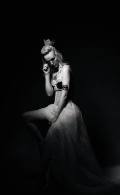 Açık renk elbiseli zarif bir kadın karanlık bir arkaplanda poz veriyor. Bir kadın akıcı bir elbiseyle zarif bir poz verir, gösterişli bir zarafet ve duygusallık