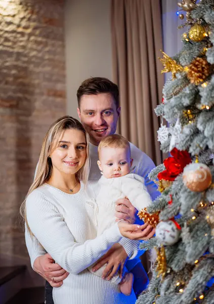 stock image Family celebrates Christmas joyfully by the decorated tree with baby. A happy family gathers around a beautifully adorned Christmas tree