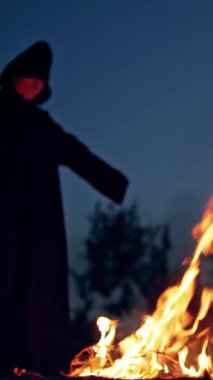Şenlik ateşinin yanındaki siyahlı cadı. Şenlik ateşinin etrafında dolaşan mistik cadı. Dikey video