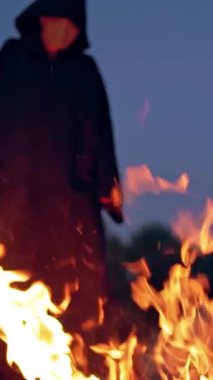 Cadı şenlik ateşinin yanında hokkabazlık yapıyor. Şenlik ateşinin yanındaki korkunç cadıyı kapatın. Dikey video