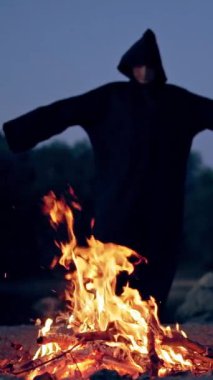 Şenlik ateşinin yanındaki siyahlı cadı. Şenlik ateşinin etrafında dolaşan mistik cadı. Dikey video