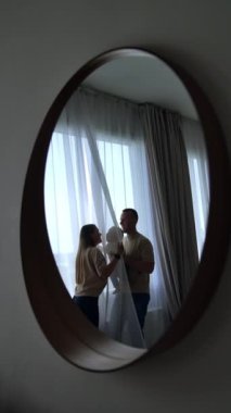 Bebekli genç bir ailenin ayna yansıması. Ebeveynler sevgili çocuklarını sevgiyle öpüp oynarlar. Dikey video.