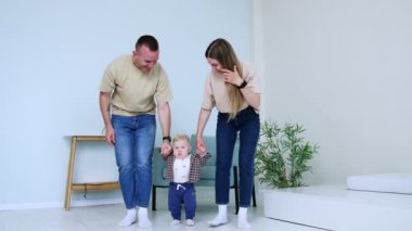 Ebeveynler yere basan küçük bebeklerinin ellerini tutarlar. Anne ve baba oğullarına yürümeyi öğretiyor..