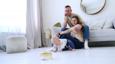 Sevgi dolu ebeveynler oturup sevimli bebeklerini seyrederler. Küçük çocuk yerdeki bir noktayla meşgul. Önündeki pastaya dikkat etmiyor..