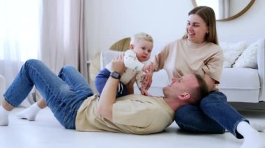 Gülümseyen beyaz bir adam, karısının dizlerinin üzerinde yere yatar. Baba karnının üstünde tombul bir erkek çocuğu tutuyor. Evde mutlu bir aile.