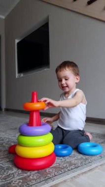Enerjik Kafkasyalı çocuk yere bir piramit inşa ediyor. Evde oyuncaklarla oynayan tatlı bir erkek bebek. Dikey video.