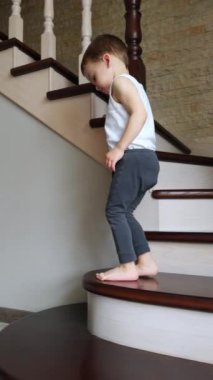 Evdeki merdivenlerden inip çıkan iki yaşında tatlı bir çocuk var. Çocuk merdivenlerde oturur ve bir şeyin sıkıştığı ayağa bakar. Dikey video.