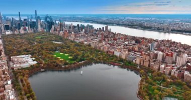 New York şehir merkezindeki yeşil Central Park 'taki bir göletin manzarasına yaklaşıyoruz. Şehrin engin manzarası. Arkaplanda Doğu Nehri var. Üst görünüm.