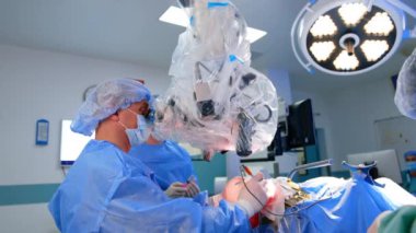 Profesyonel beyin cerrahı mikroskoba bakarak ameliyat yapıyor. Arkaplanda şırınga tutan bir doktora yardım etmek.