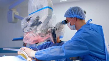 Beyin cerrahları plastikle kaplı mikroskoba bakarlar. Doktorlar işlemleri gelişmiş ekipmanlar kullanarak gerçekleştirir.