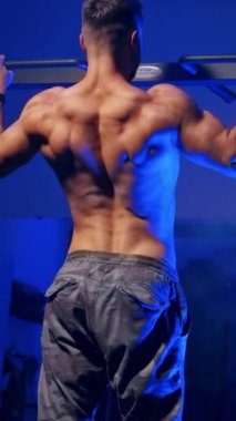 Spor salonundaki yatay barda antrenman yapan bir adam. Arka plan portresi, kapalı alanda barfiks çeken genç vücut geliştiricisinin. Dikey video