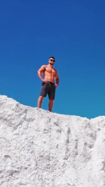 Sporcu dağın yamacında duruyor. Çıplak gövdeli bir adam dağın tepesinde duruyor ve doğanın tadını çıkarıyor. Dikey video