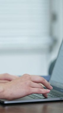 Evde dizüstü bilgisayar kullanan bir kadın. Ev ofisinde çalışan, elini klavyeye koyan kadına yakın dur. Dikey video