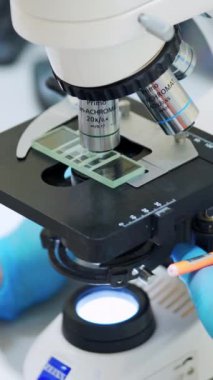 Kanın laboratuvar incelemesi. Laboratuvarda mikroskopla çalışan üniformalı kadın bilim adamlarına yakın çekim. Dikey video