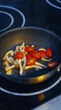 Kızartma tavasında biraz mantar kızartılır. Kızartmaya taze domates ekleniyor. Kapatın. Dikey video.