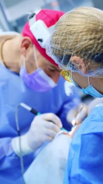 Doktor hastanın üzerine eğildi ve tiroidi dikkatlice ameliyat etti. Sarı koruyucu gözlük takan kadın hemşire ameliyatta yardımcı oluyor. Dikey video.