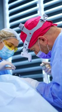 Beyaz erkek doktor ve kadın hemşire tiroid üzerinde çalışıyorlar. Başhekim prosedürde cerrahi aletleri dikkatlice kullanır. Dikey video.
