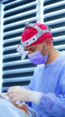 Erkek doktor ameliyatta olan bir hastanın başında duruyor. Cerrah prosedürde iplik ve pens kullanır. Dikey video.