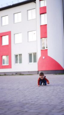 Erkek bebek dışarıdaki fayansların yanında dördünün üzerinde sürünüyor. Çocuk yarı yolda durup kameraya yaklaşıyor. Dikey video.