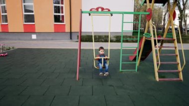 Tatlı çocuk salıncakta yavaşça sallanıyor ve kendini itiyor. İki yaşında bir çocuk oyun alanında vakit geçiriyor..