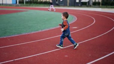 Aktif çocuk stadyumun yanından koşup topa yaklaşıyor. İki yaşında bir çocuk spor öğreniyor ve yaşam tarzına uygun..