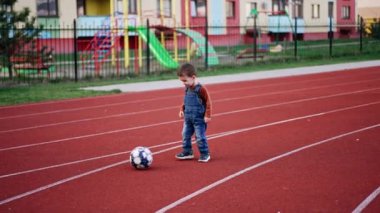 Kot pantolonlu çocuk stadyumun orada topa vuruyor. Küçük çocuk futbol oynamayı öğreniyor..