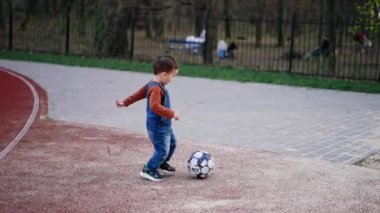 Stadyumun yanından geçen topu takip eden beyaz bir çocuk. Bebek dışarıda eğleniyor..
