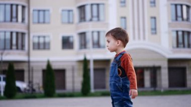 Kot pantolon giyen sevimli bebek dışarıda duruyor. Çocuk parmaklarını göstererek kameraya döndü. Bulanık arkaplan.