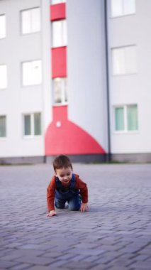 Erkek bebek asfalt yolda sürünen kameraya yaklaşıyor. Yürüyüşe çıkan komik çocuk. Dikey video.