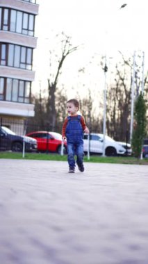 Küçük oğlan şehir sokaklarında yürüyor. Kot pantolonlu çocuk çok katlı binanın yanındaki asfalt zeminin yanından geçiyor..