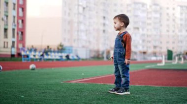 Sevimli çocuk topunu stadyuma götürmek için koşuyor. Küçük çocuk dışarıda spor oynuyor..