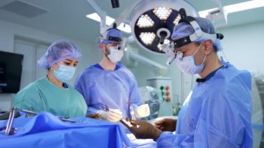 Cerrahi lensler takan beyin cerrahı metal bir alet tutuyor. Hemşireye yardım etmek, aletleri doktora verir..
