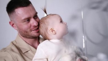 Sakallı, beyaz bir adam elinde güzel bir bebek tutuyor. Aktif çocuk balonu yakalamak için eğiliyor. Kapat..