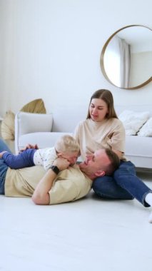 Göğsünde bir bebek taşıyan bir adam karısının dizlerinin üzerine çöker. Güzel beyaz bir aile birlikte vakit geçiriyor. Dikey video.
