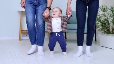 Kot giyen tanınmamış ebeveynler yeni yürümeye başlayan oğullarını tutuyorlar. Sevimli, tatlı erkek bebek yürümeyi öğreniyor..