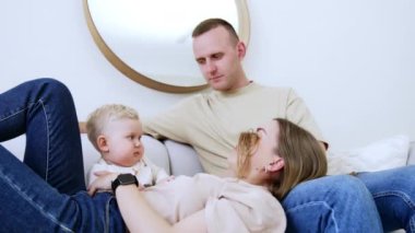 Anne yüzünü bir bebekten saçının arkasına saklar. Gülümseyen çocuk annesinin yüzünü ortaya çıkarıyor. Babam gülümseyerek izliyor. Ailecek vakit geçirmek..