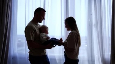 Sevgi dolu beyaz anne ve babalar pencerenin kenarında sevgili bebeklerini tutuyorlar. Evde birlikte güzel bir aile..