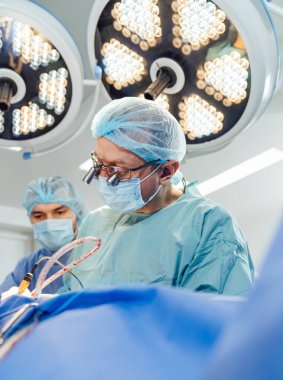 Cerrahlar modern bir cerrahi tiyatroda hassas bir ameliyat yapıyorlar. İki cerrah parlak ameliyat sırasında cerrahi bir prosedüre odaklanır