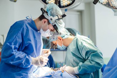 Cerrahlar modern bir ameliyathanede karmaşık bir ameliyat yapıyorlar. İki cerrah, iyi donanımlı bir cerrahi süitte hassas bir prosedür uygularken dikkatle odaklanır..