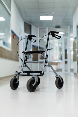 Compact walker positioned in a bright hospital corridor. A sturdy walker awaits use in a spacious hospital corridor filled with light. clipart